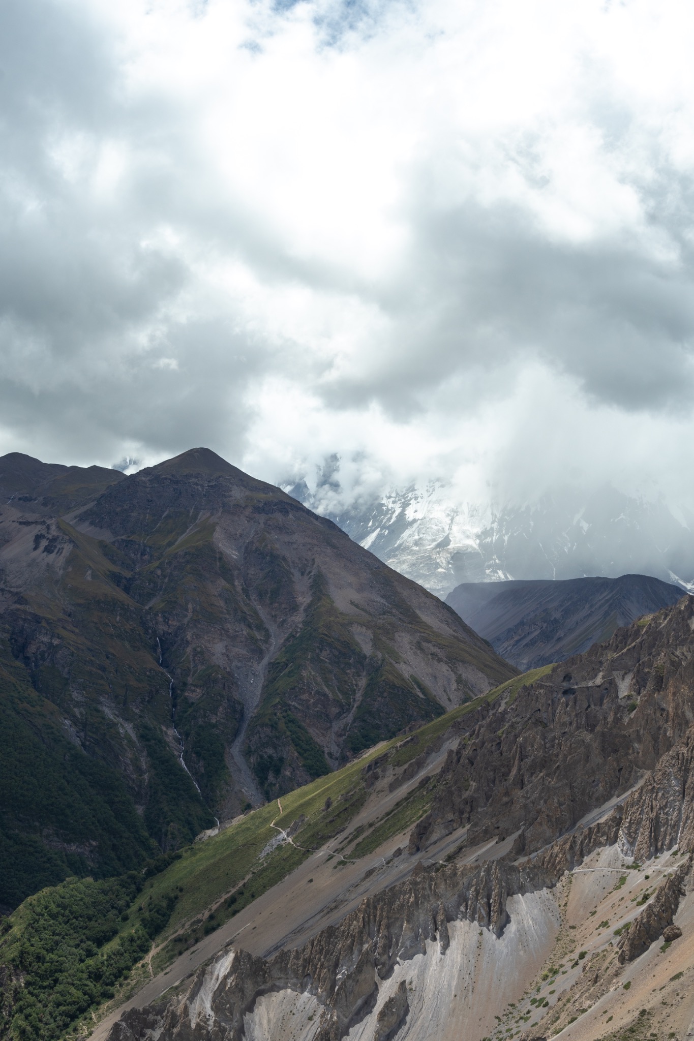 A narrow trail crossing steep mountain ridges beneath low clouds